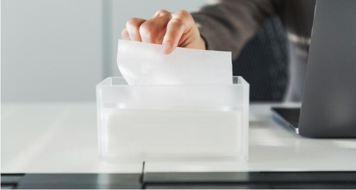 Sick worker at desk taking tissue out of box