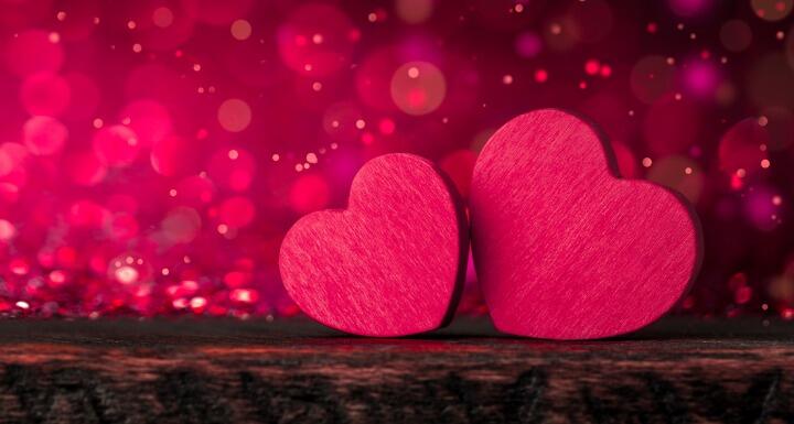 Two pink wooden hearts sitting on a brown wooden table with pink glitter falling in the background