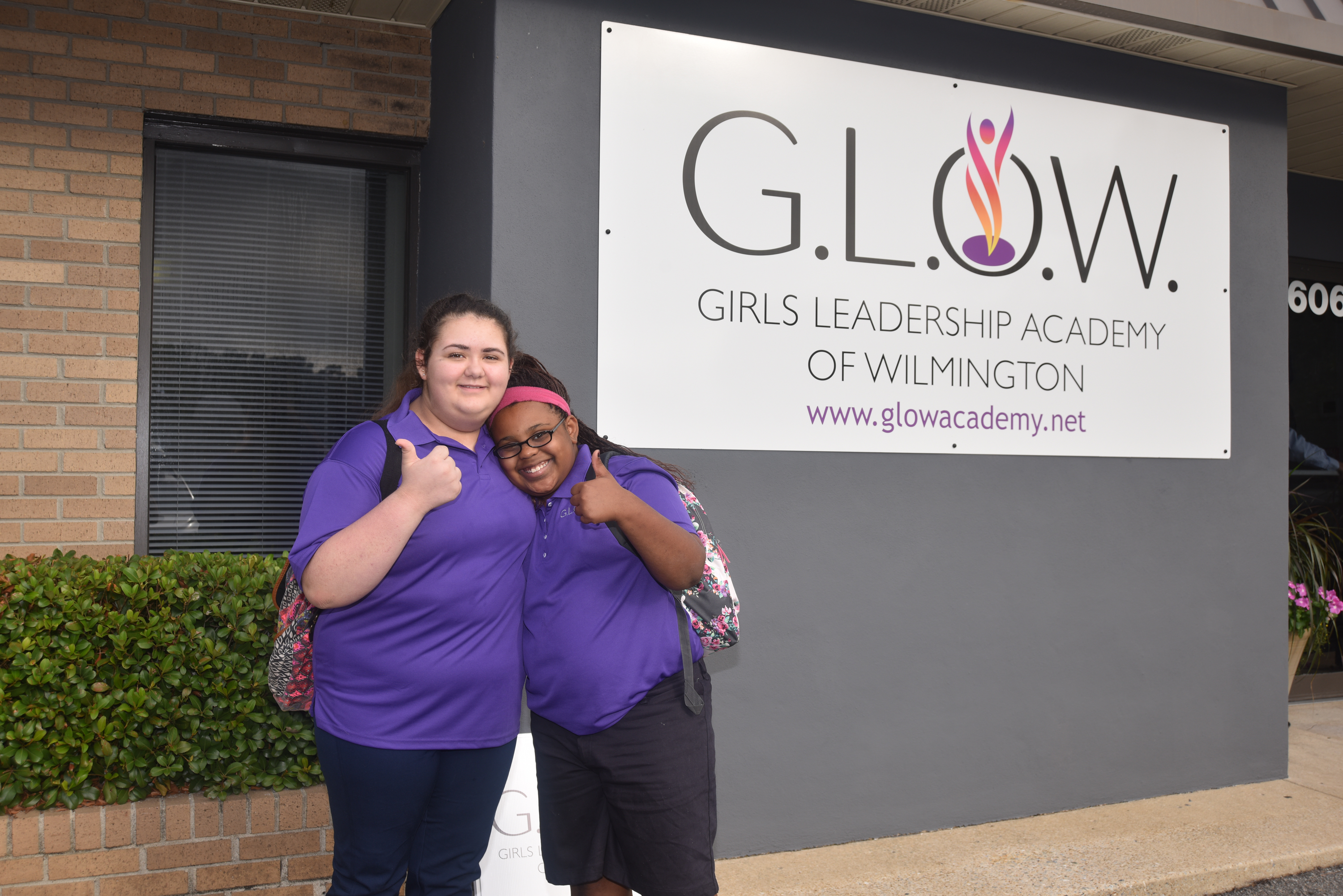GLOW students proudly pose in front of the Academy logo.