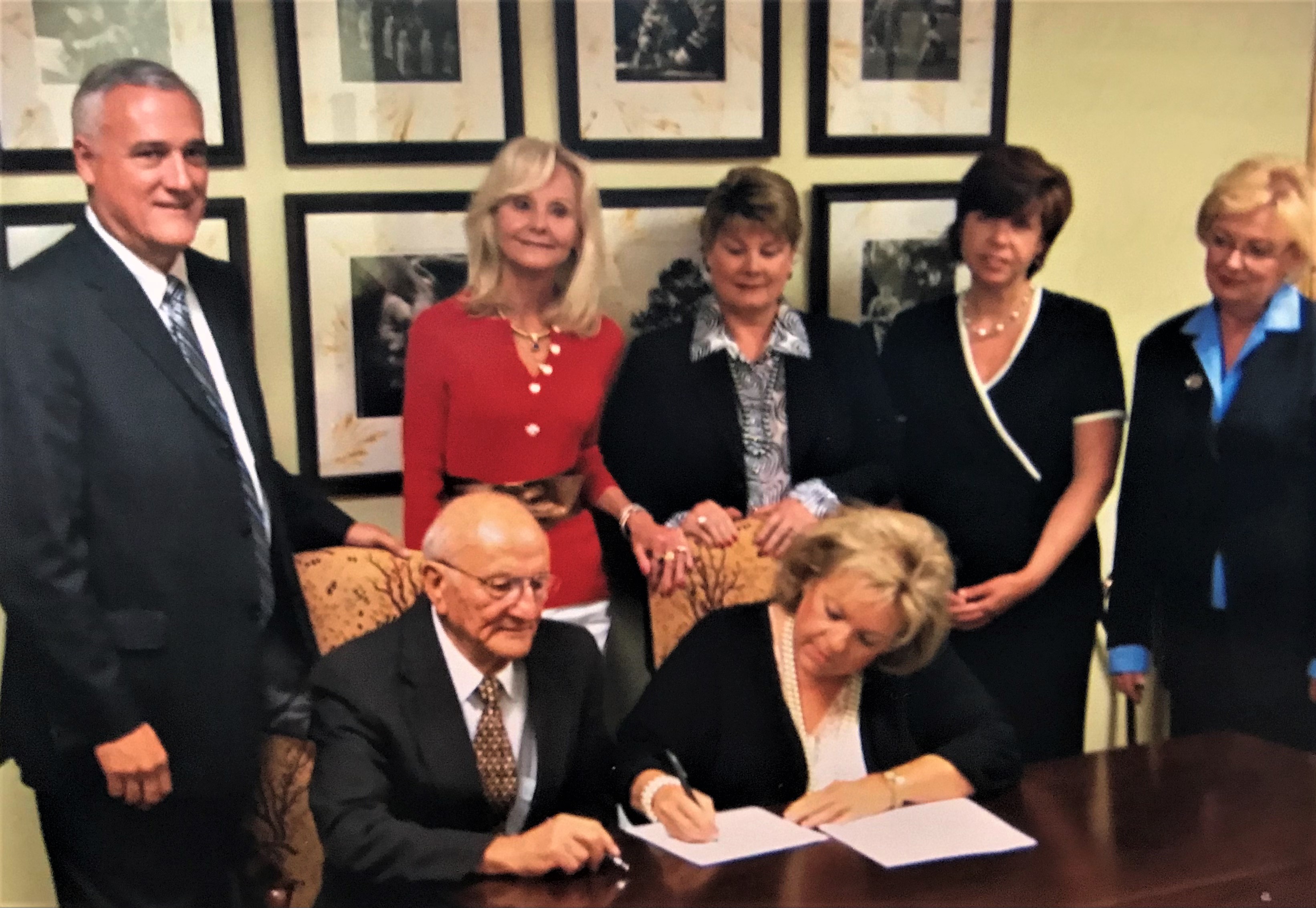 Kelli Moore Barham signs the paperwork to establish the George A. Kahdy Enloe High School Alumni Scholarship Endowment in 2007 with Mr. Kahdy, seated left. Standing behind them are Bill Baxley, Debra Hooper, Pat Godwin Long, Jennifer Tolle Whiteside and Kaye Lloyd Gattis. All are former Enloe students with the exception of Whiteside, who is NCCF’s President & CEO.