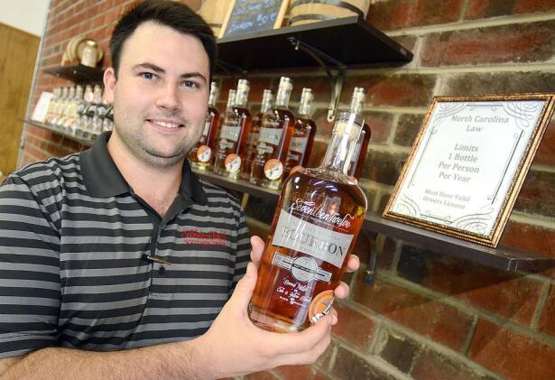 Zackary Cranford co-owner of Foothills Distillery in Conover, holds a bottle of Seventeen Twelve Bourbon, which is one of three spirits he can sell straight from the distillery. (Image - Robert C. Reed)